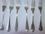 six forks and a spoon on a white table