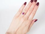 woman ' s hand with red manicured nails holding a ring with a ruby stone