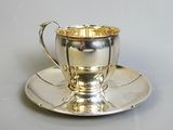 a silver cup and saucer sitting on a saucer