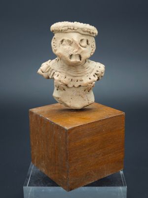 une figurine en céramique blanche représentant un homme coiffé d'un chapeau, posée sur un bloc de bois