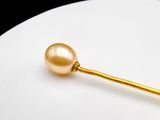 a golden pearl on a gold stick on a white plate