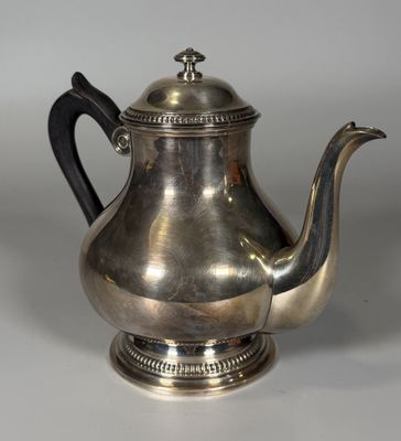 une théière ancienne en argent avec une poignée noire sur une surface blanche