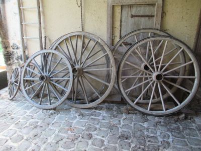 trois vieilles roues de wagon en bois adossées à un mur