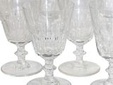 six clear wine glasses are lined up in a row on a white surface
