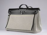 a beige and black bag with a black handle on a white surface