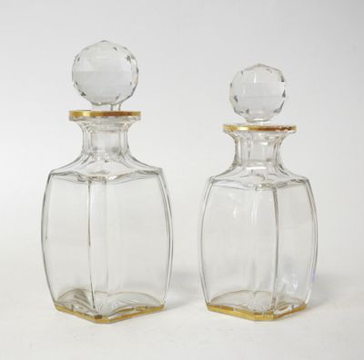 two clear glass bottles with gold rims on a white surface