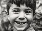 photographie en noir et blanc d'un jeune garçon souriant devant un mur de pierre