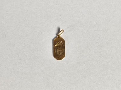 un petit pendentif en or représentant un visage, posé sur un fond blanc