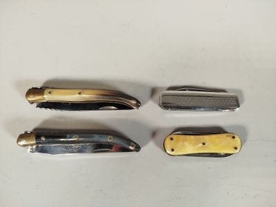 quatre types différents de couteaux de poche posés sur une surface blanche