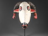 un masque blanc et rouge muni de cornes, posé sur un socle noir