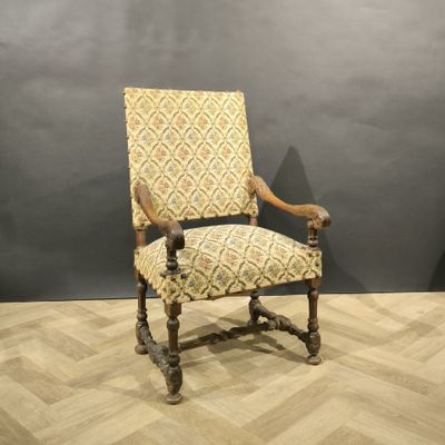 une vieille chaise en bois dont le dossier et les accoudoirs sont recouverts d'un tissu à motifs