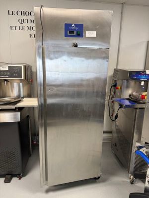 un réfrigérateur en acier inoxydable dans une cuisine, avec d'autres appareils électroménagers en arrière-plan