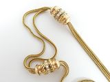 gold plated necklace with a long chain and a tassel on a white surface