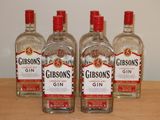 trois bouteilles de gin posées sur une table en bois, avec un mur blanc en arrière-plan