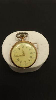 a gold pocket watch sitting on a white stand