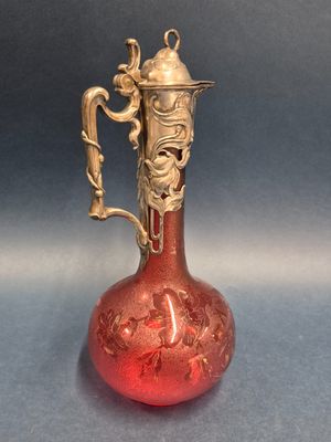 un vase en verre rouge muni d'une anse dorée, posé sur une table