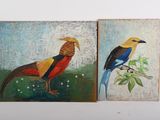 two paintings of birds painted on wooden boards sitting on a table