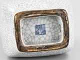 a close up of a white and gold vase with a blue square in the center