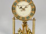 a gold clock on a stand with bells on it
