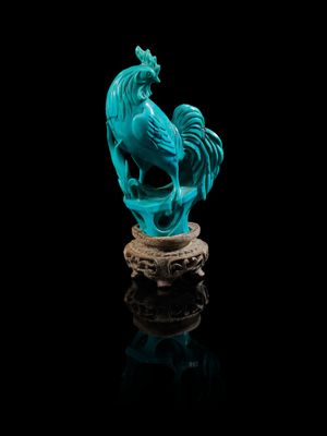 une statue bleue représentant un coq posé sur un rocher, sur fond noir