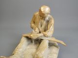 une statue représentant un homme assis sur un rocher, en train de lire un livre