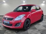 Une Suzuki Swift rouge est garée dans une pièce au sol à carreaux.