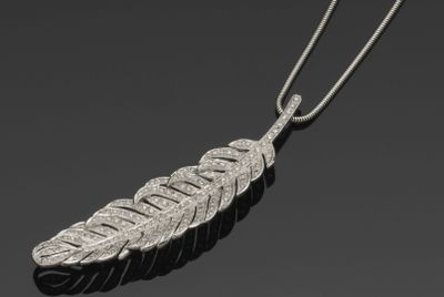 un pendentif en forme de plume argentée avec une chaîne, sur fond noir