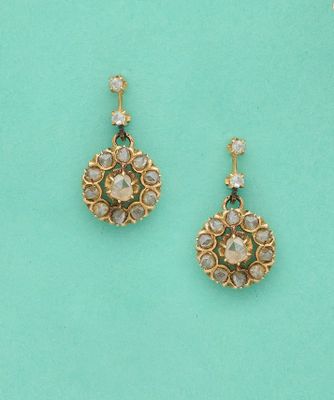 une paire de boucles d'oreilles dorées ornées de pierres blanches sur fond turquoise