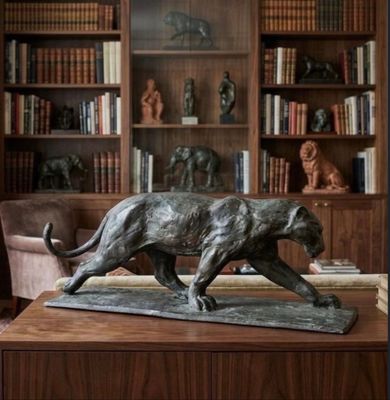 a statue of a cat on a table in front of a bookshelf