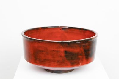 un bol rouge et noir posé sur un socle blanc
