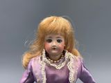 a doll that is wearing a purple dress and a pearl necklace