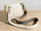 beige and white purse on a wooden table with a gray strap