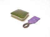 un ruban violet et un petit étui vert posés sur une surface blanche