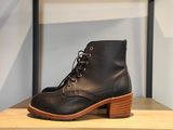 un gros plan sur une paire de bottes noires posées sur une étagère en bois