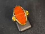 une image représentant une bague ornée d'une pierre orange posée sur un support en métal