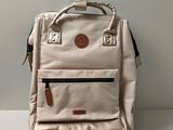 beige backpack sitting on top of a white table next to a white wall