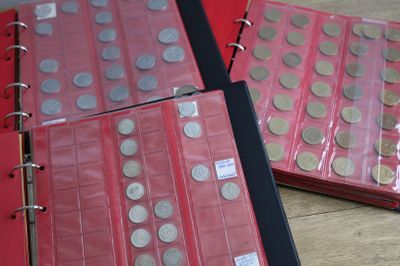 trois classeurs rouges contenant des pièces de monnaie, posés sur une table en bois