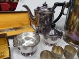 a silver tea pot and silver cups on a table