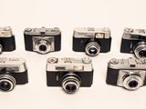 six old cameras are lined up in a row on a white surface