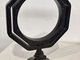 un miroir octogonal noir posé sur un pied, sur une table blanche