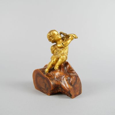 gold figurine of a boy playing a flute on a rock