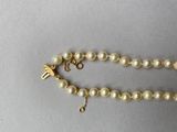 an image of a pearl necklace with a gold clasp on a gray surface
