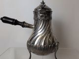 a silver coffee pot with a handle on a glass table