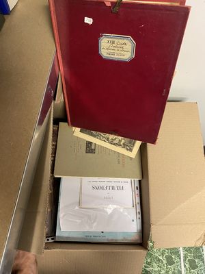 une boîte rouge posée sur une table, contenant des papiers et un dossier