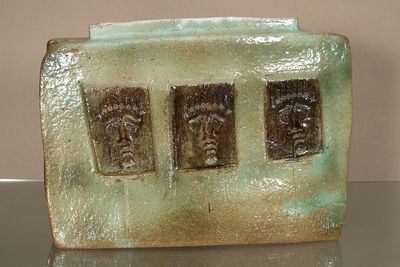 une sculpture en céramique représentant trois visages, posée sur une assiette verte