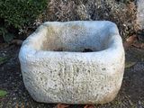 a stone bowl sitting on the ground next to a bush