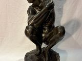 bronze statue of a man sitting on a rock with his hands on his knees