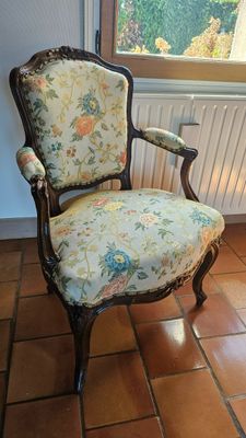 une chaise dont l'assise est recouverte d'un tissu à motifs floraux, placée devant une fenêtre