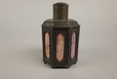 un petit vase avec un couvercle posé sur une surface blanche