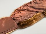 une image représentant une veste marron à col en fourrure posée sur une surface blanche